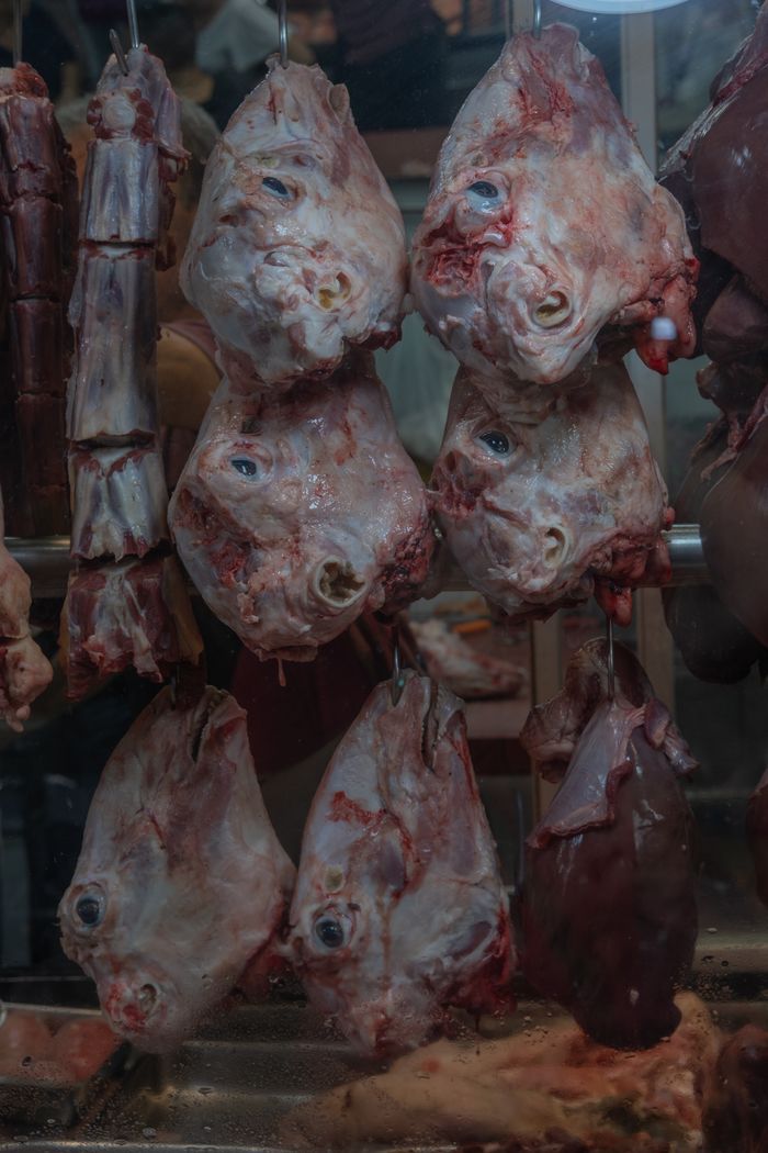 programs-01 A vivid display of raw meat heads hanging at a butcher's stall, showcasing traditional market setting.