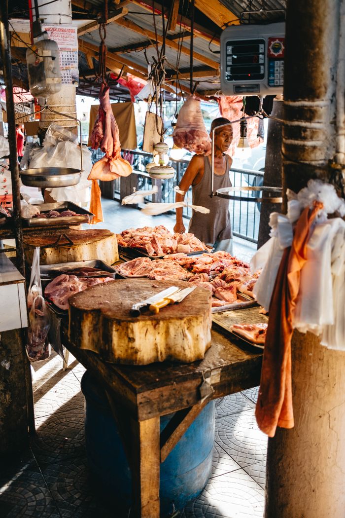 A lively urban market scene with a butcher preparing fresh meat on a wooden table.