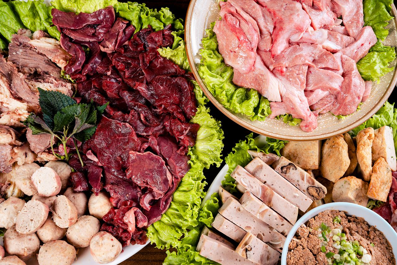programs-01 An overhead view of assorted raw meats and ingredients on platters with lettuce.