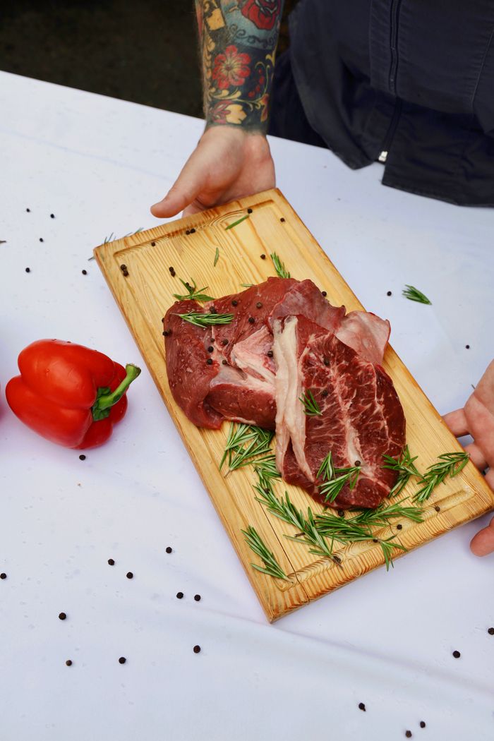 Fresh beef steaks seasoned with rosemary on a wooden board.