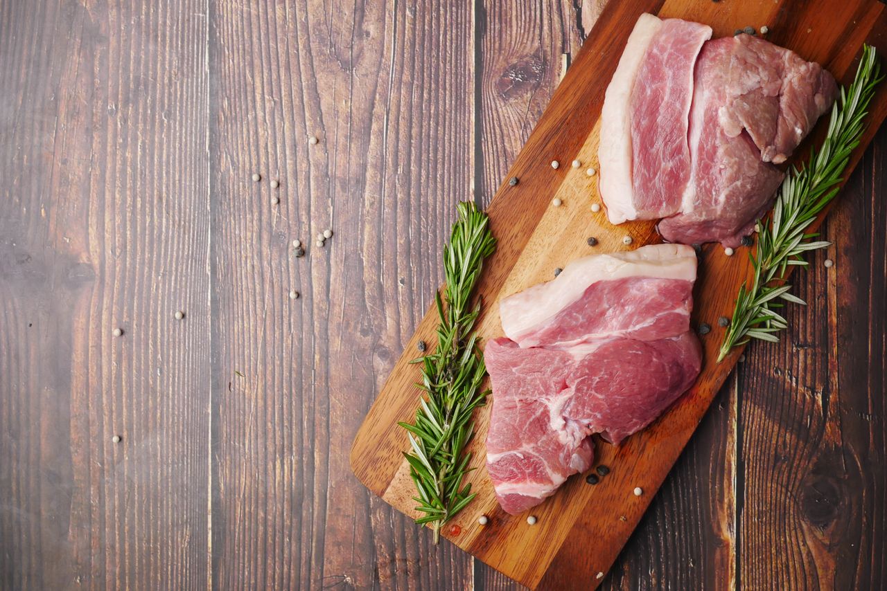 High-quality image of raw pork cuts with rosemary on a rustic wooden board, perfect for culinary themes.